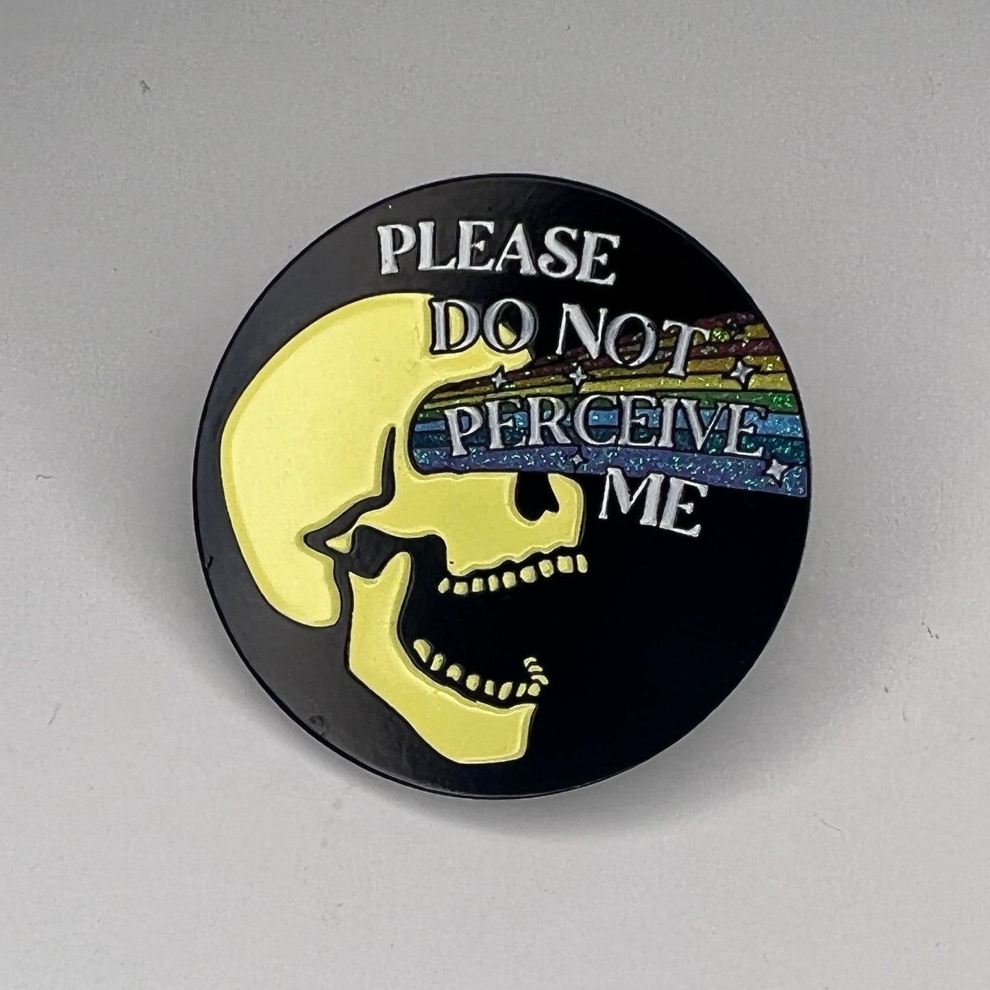 Round pin with text 'Please do not perceive me' on a gray background