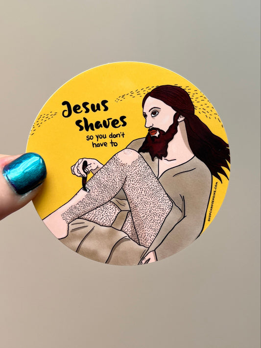 Circular sticker with illustration of a bearded baddie and text 'Jesus Shaves' held by a hand with blue nail polish.