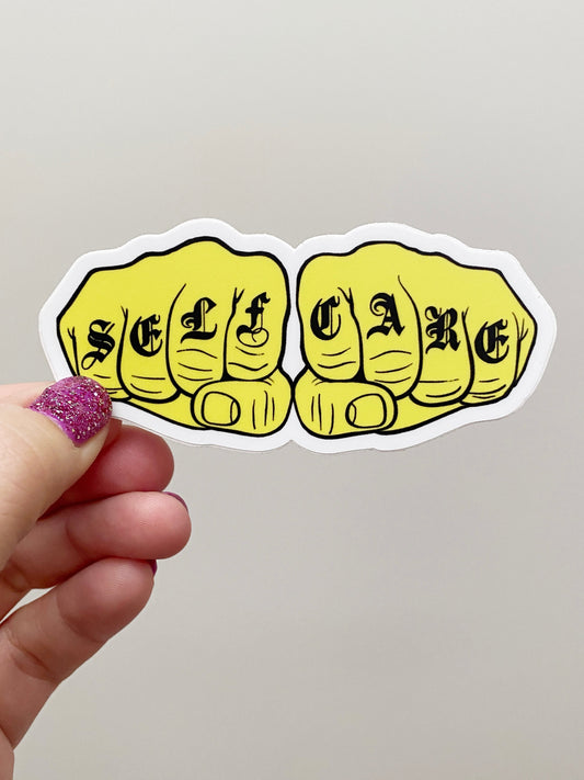 Hand holding a yellow 'SELF CARE' sticker with fists on a plain background