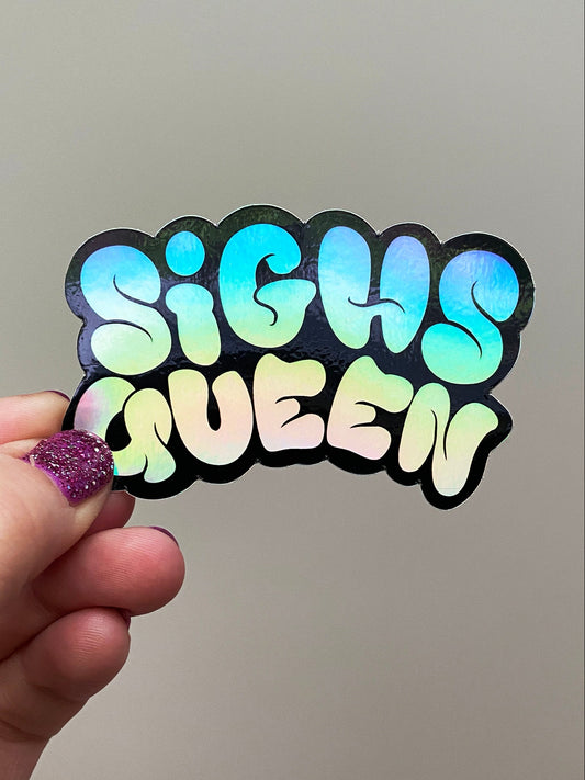 Holographic 'Sighs Queen' sticker held by a hand against a plain background