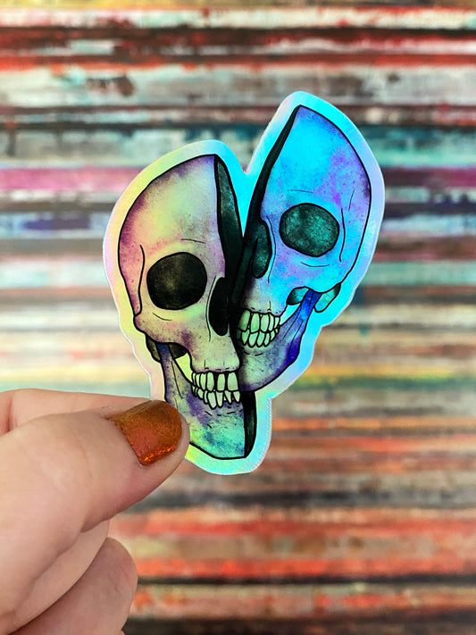 Holographic skull sticker held by a hand against a colorful striped background