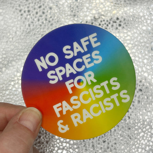 Round sticker with text 'No safe spaces for fascists & racists' held by a hand against a textured background