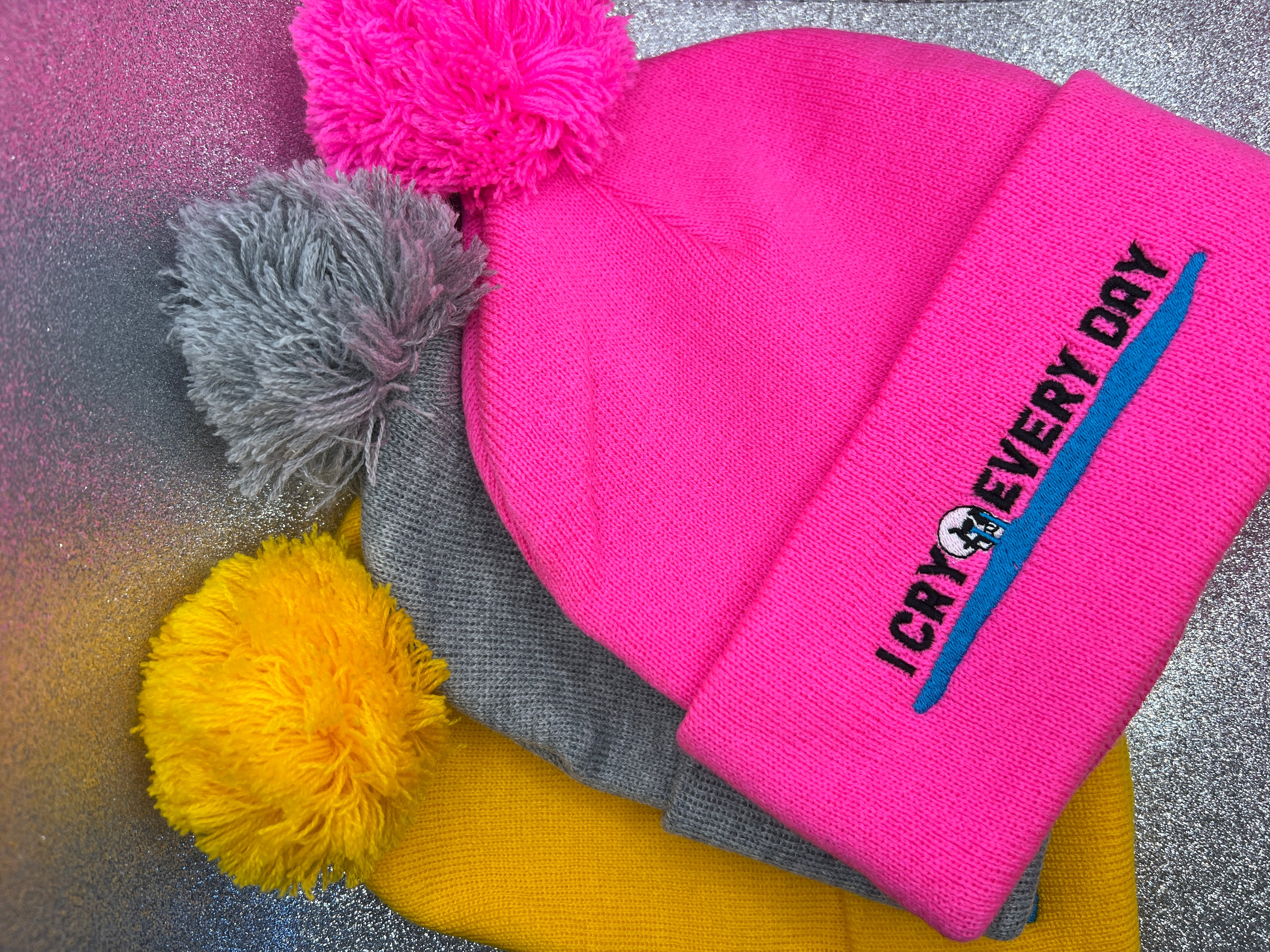 Pink beanie with pom-poms on a textured surface