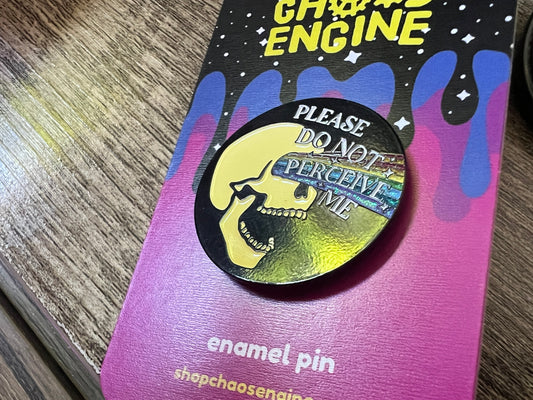 Enamel pin with skull design and text on a colorful card, brand 'Chaos Engine' visible.