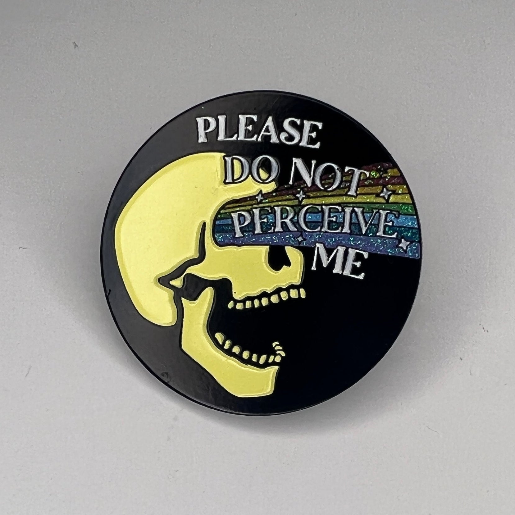 Round pin with text 'Please do not perceive me' on a gray background