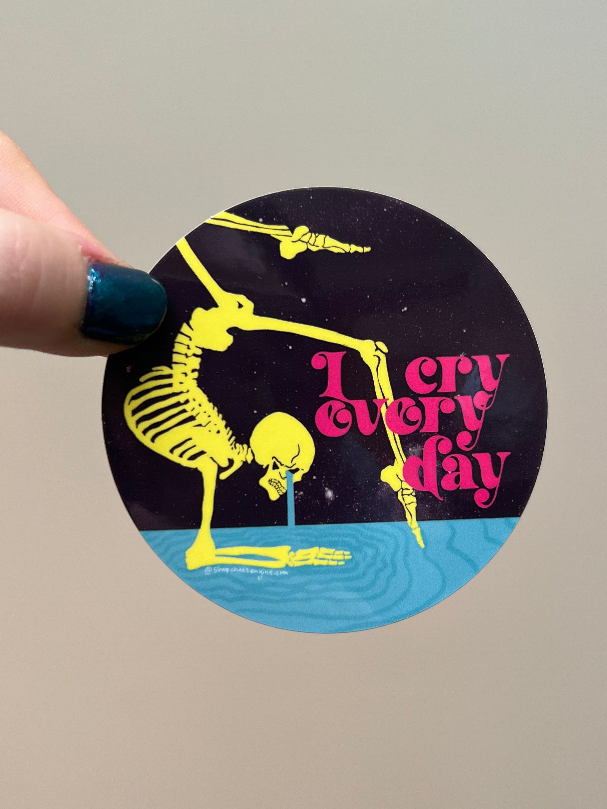 Circular sticker with skeleton design and text held by a hand against a plain background