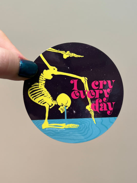 Circular sticker with skeleton design and text held by a hand against a plain background