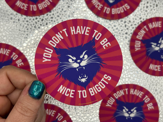 Sticker with a cat illustration and text 'You don't have to be nice to bigots' held by a hand.
