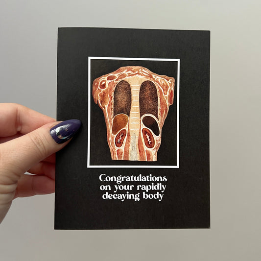 Card with anatomical illustration and humorous text held by a hand against a plain background