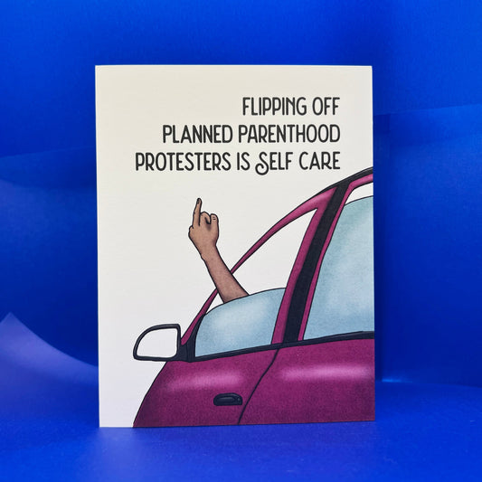 Card with a hand flipping the middle finger out of a car window, text 'Flipping off Planned Parenthood protesters is self care' on a blue background.
