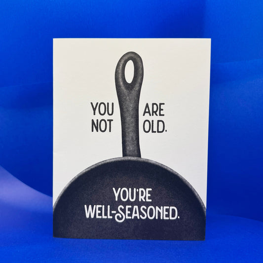 Card with a black frying pan illustration and humorous text on a blue background